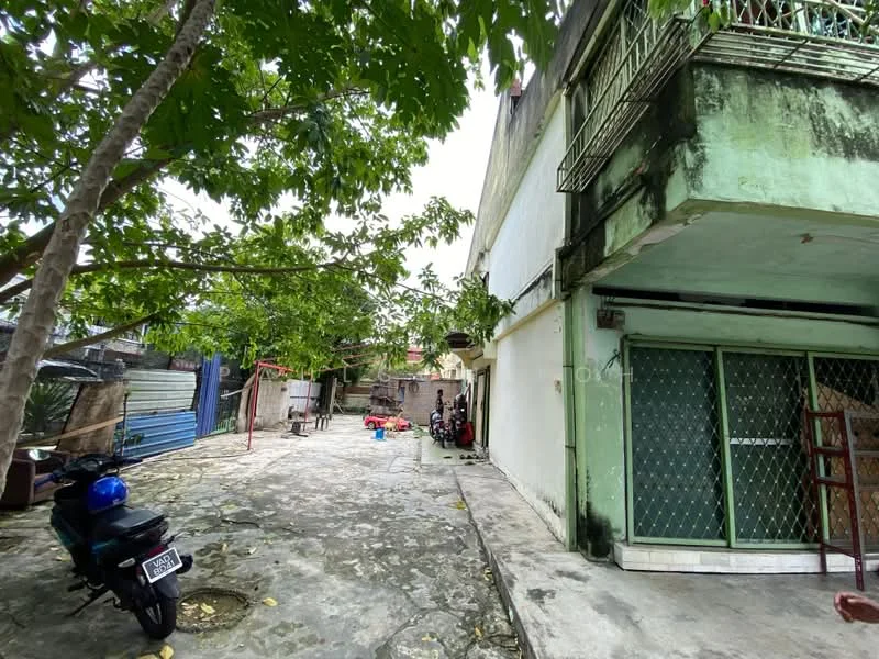 Exterior type: detached bungalow; features: two-storey building, exposed concrete facade, green exterior paint, balcony with railing, stone-paved walkway, mature trees, open courtyard area, motorcycle parked, outdoor space for activities; style: traditional.