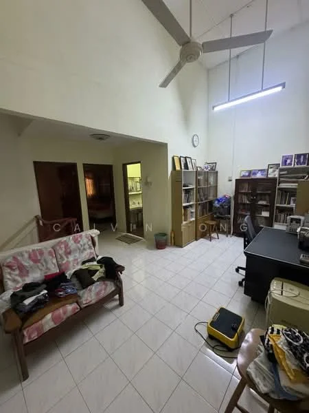 Living features: white painted walls, tiled flooring, 5-blade ceiling fan, large bookshelf, wooden sofa with floral upholstery, coffee table, desk with chair, decorative wall clock, overhead fluorescent lighting. Room features: doorway leading to another room, visible laundry items on sofa.