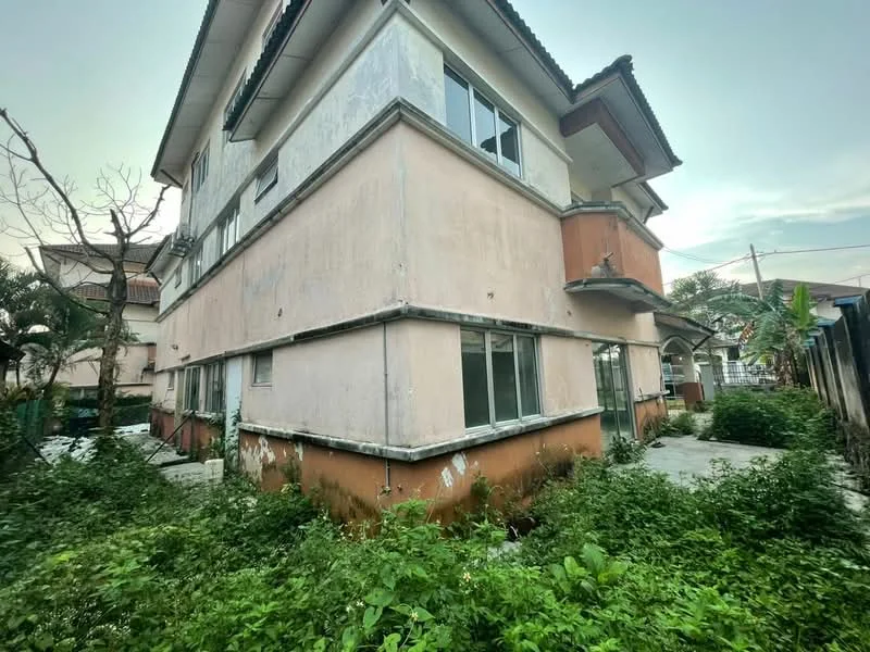 Exterior type: semi-detached house; features: two-storey building, exposed concrete facade, white painted facade, brown painted lower section, multiple windows, overgrown garden, concrete pathway, roof overhang, surrounded by greenery; style: traditional.