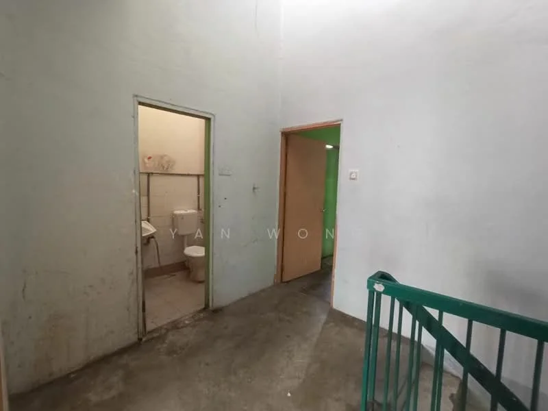 Room features: plain white walls, concrete flooring, staircase with green railing, doorway to bathroom, doorway to another room, light switch, no visible windows; style: minimalist.