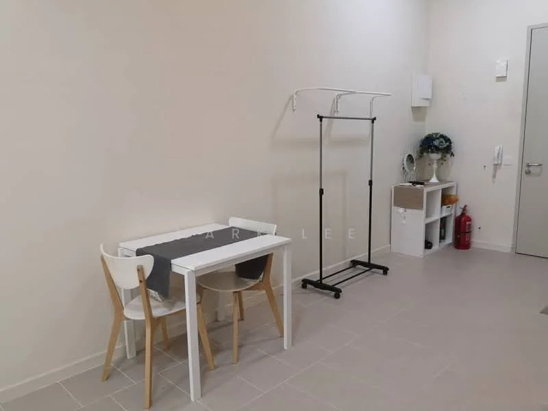 Room features: white painted walls, light grey tile flooring, small white dining table, two chairs (one white, one wooden), clothing rack, small white shelving unit, decorative plant on shelf, fire extinguisher, door with handle, wall-mounted electrical panel; style: minimalist.