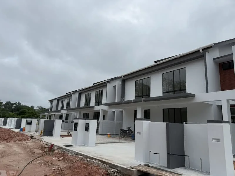 Exterior type: linked terrace house; features: white painted facade, large floor-to-ceiling windows, flat roof, two-storey structure, concrete driveway, unfinished landscaping, visible construction materials, motorbike parked in front, grey accent walls, gated entry, surrounded by open land; style: modern.