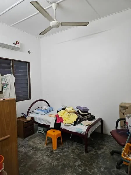 Bedroom features: single bed with mattress, 5-blade ceiling fan, white painted walls, concrete flooring, wooden wardrobe, wooden bedside table, stack of clothes on bed, orange plastic stool, office chair, window with dark frame, box in corner.