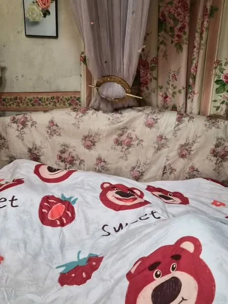 Room features: floral patterned upholstery, white bedding with bear and strawberry prints, curtains with floral design, wall with floral wallpaper, decorative wall art, wooden curtain rod, soft furnishings; style: traditional.