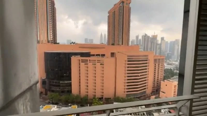 Exterior type: high-rise condominium; features: glass curtain wall, orange painted facade, surrounded by urban skyline, view of Petronas Twin Towers, multiple-storey structure, balconies visible, adjacent to commercial buildings; style: modern.