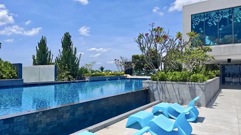 Exterior type: swimming pool deck; features: infinity pool, pool deck with loungers, landscaped garden with tropical plants, stone-paved walkway, modern building facade with large windows, surrounded by greenery, clear blue sky; style: modern.