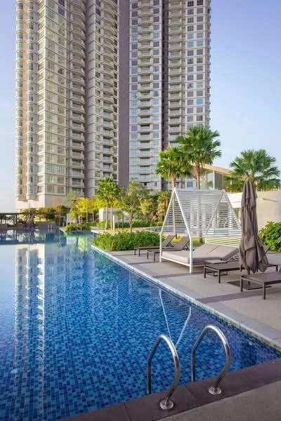 Exterior type: high-rise condominium; features: infinity pool, pool deck with loungers, tropical landscaping, palm trees, manicured lawn, glass curtain wall facade, recessed balconies, approximately 20-storey high-rise; style: modern.