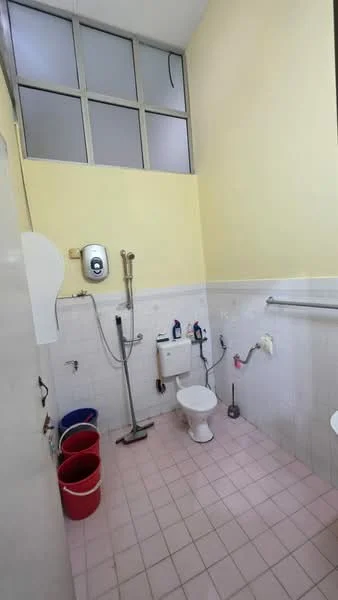 Bathroom features: yellow painted walls, white tiled walls, pink tiled flooring, one-piece toilet, shower with wall-mounted faucet, water heater, grab bar, two wall-mounted shelves, three red plastic buckets.