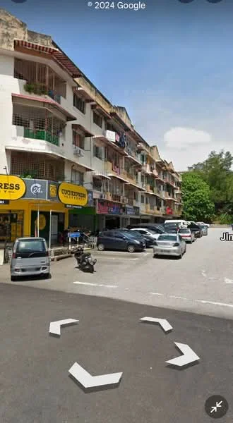 Exterior type: low-rise apartment block; features: multi-storey building, balconies with railings, commercial units on ground floor, parking area with multiple cars, street view, surrounded by greenery, signage for businesses, concrete facade, visible awnings over shops; style: modern.