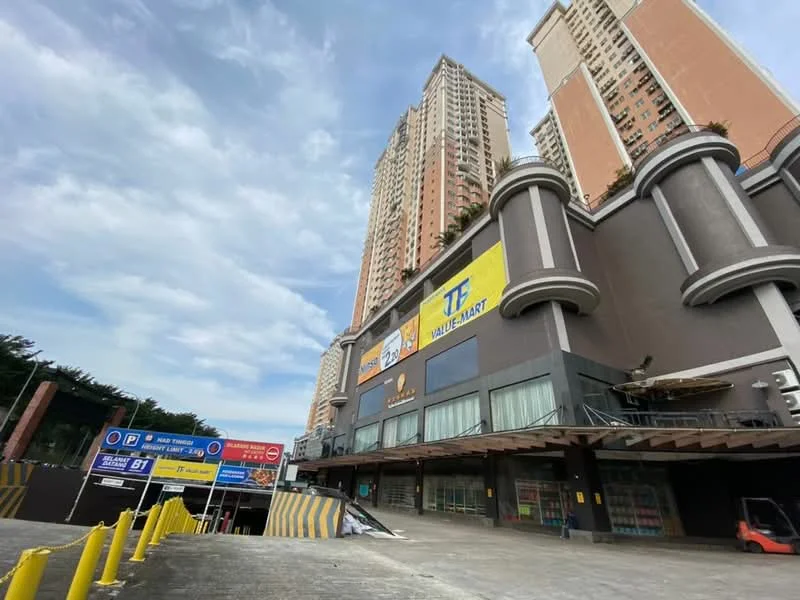 Exterior type: high-rise condominium; features: glass curtain wall, exposed concrete facade, large advertising signage, multiple storeys, parking entrance, manicured landscaping, surrounding greenery; style: modern.