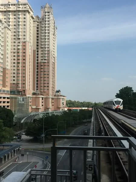 Exterior type: high-rise condominium; features: glass curtain wall, pink painted facade, recessed balconies, surrounded by greenery, adjacent to train tracks, urban context with road view; style: modern.