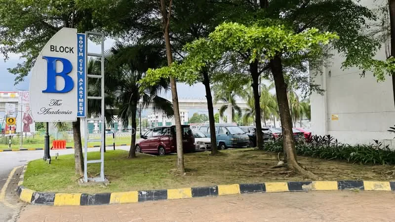 Exterior type: low-rise apartment block; features: signage with 'BLOCK B' and 'The Academia', landscaped area with grass, palm trees, parking lot with visible cars, curved driveway, yellow and black striped curb, surrounding greenery; style: modern.