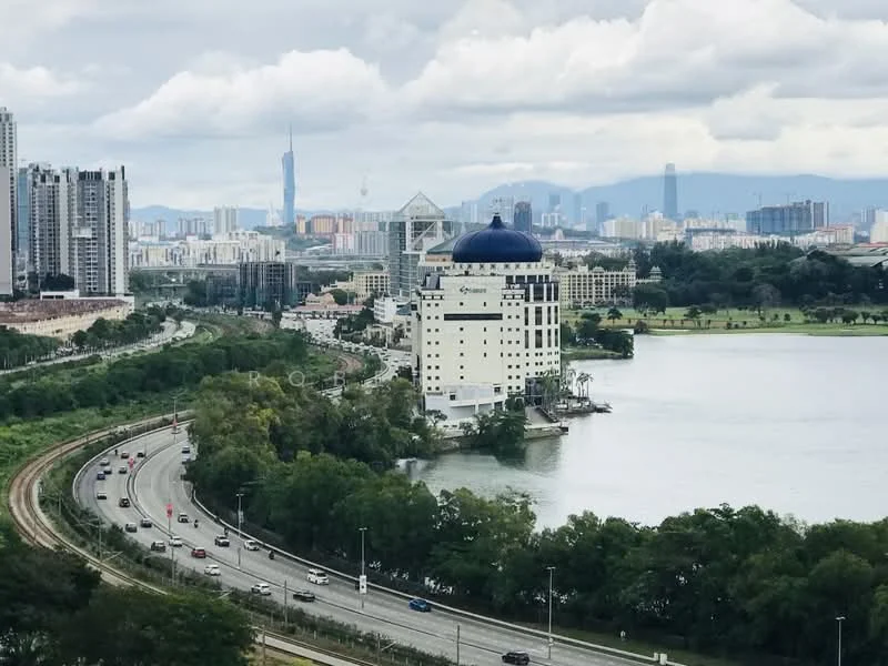 Exterior features: waterfront view, city skyline in background, road alongside water, greenery along the water's edge, high-rise buildings in distance, cloudy sky; style: modern.
