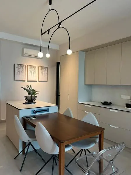 Kitchen features: white cabinetry, marble countertop, island with built-in storage, 4-seater dining table, transparent dining chairs, recessed downlights, pendant lighting, wall-mounted split AC, black bowl on countertop, decorative plant on island, framed artwork on walls, grey walls, light-colored flooring; style: modern.