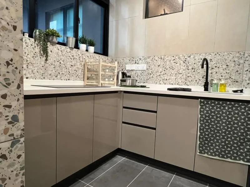Kitchen features: L-shaped kitchen layout, light grey cabinetry with flat-panel doors, white countertop, black faucet, single-bowl stainless-steel sink, built-in stove, terrazzo backsplash, grey patterned dish towel, black tile flooring, window with natural light, decorative plants on countertop, open shelving with kitchenware; style: modern.