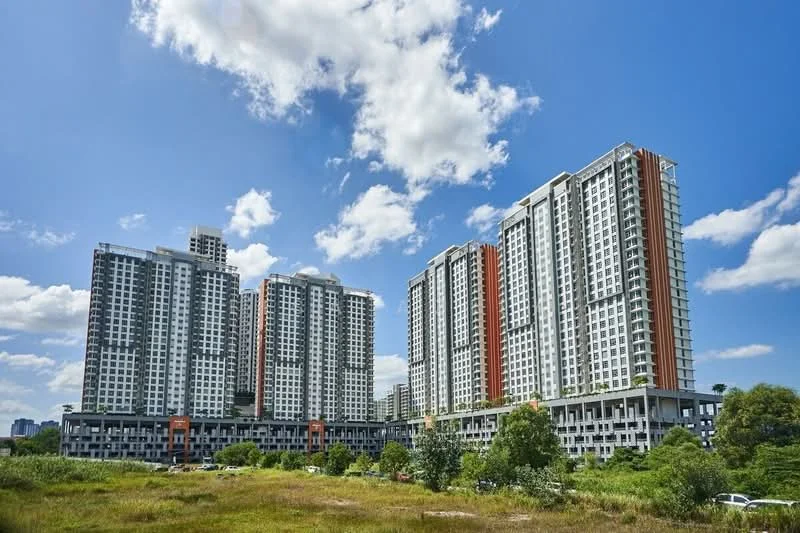 Exterior type: high-rise condominium; features: glass curtain wall, white painted facade, red accent panels, multiple storeys, landscaped grounds, surrounded by greenery, parking deck visible, balconies on upper floors; style: modern.