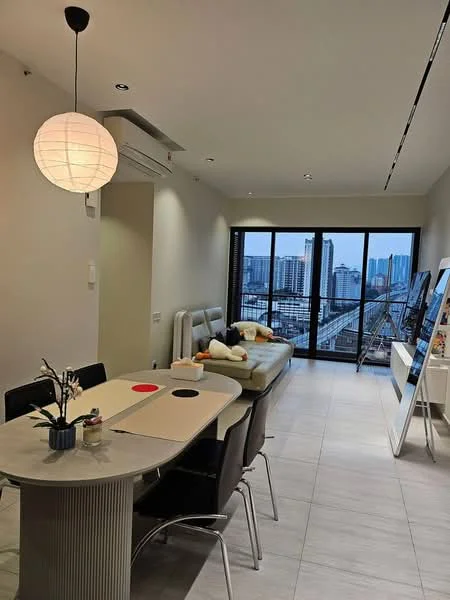 Living features: light grey sectional sofa, round dining table, black dining chairs, pendant light fixture, floor-to-ceiling windows, city skyline view, air conditioning unit, white walls, light tile flooring, decorative plant on table, wall-mounted TV, white console table; style: modern; view: city.