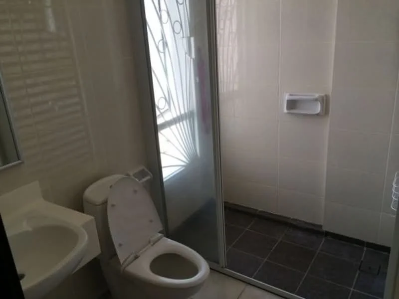 Bathroom features: white ceramic toilet, single-sink vanity with white cabinet, mirror above sink, glass shower enclosure, walk-in shower with tile cladding, black tile flooring, white wall tiles, towel rail, window with decorative grille; style: modern.