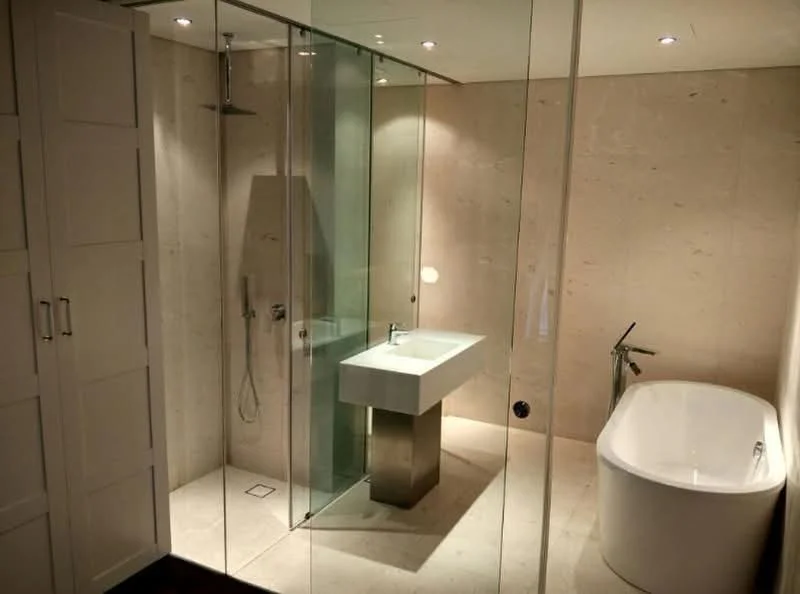 Bathroom features: freestanding bathtub, walk-in shower with glass enclosure, chrome basin mixer faucet, square sink with pedestal, stone wall cladding, marble flooring, recessed downlights, built-in cabinetry, mirror with wall-mounted light, glass shower panel; style: modern.