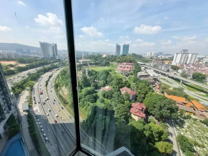 Exterior type: high-rise condominium; features: floor-to-ceiling windows, city skyline view, surrounded by greenery, adjacent to highway, urban landscape, visible road with traffic, mature trees in foreground; style: modern.