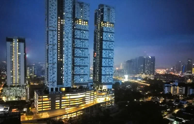 Exterior type: high-rise condominium; features: glass curtain wall, illuminated facade, multiple towers, balconies on upper floors, surrounding city skyline, nighttime lighting, landscaped ground level, urban context with city lights; style: modern.