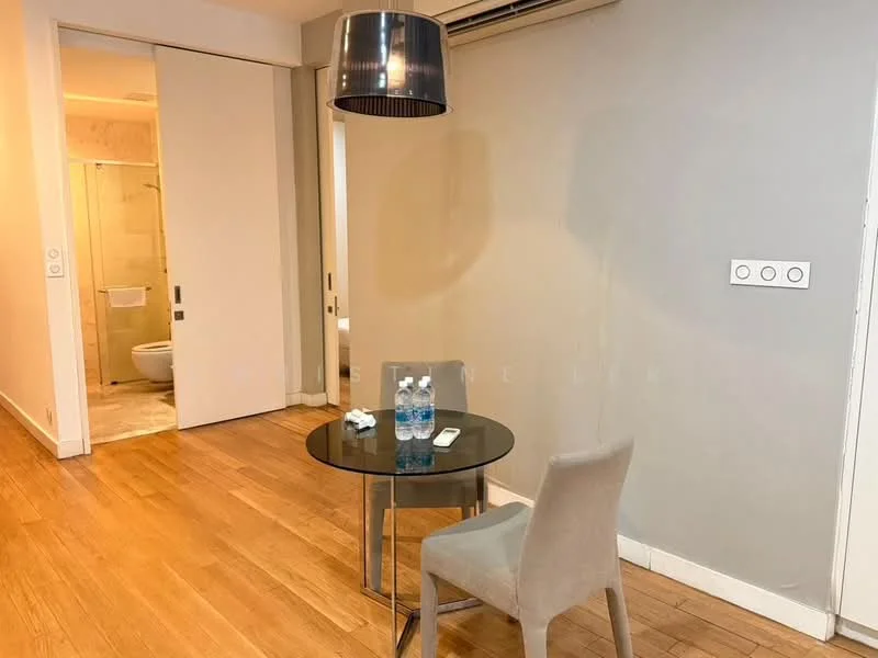 Room features: wooden flooring, grey painted walls, recessed ceiling lights, air conditioning unit, round pendant light, glass-top dining table, metal chair, water bottles on table, remote control on table; style: modern.