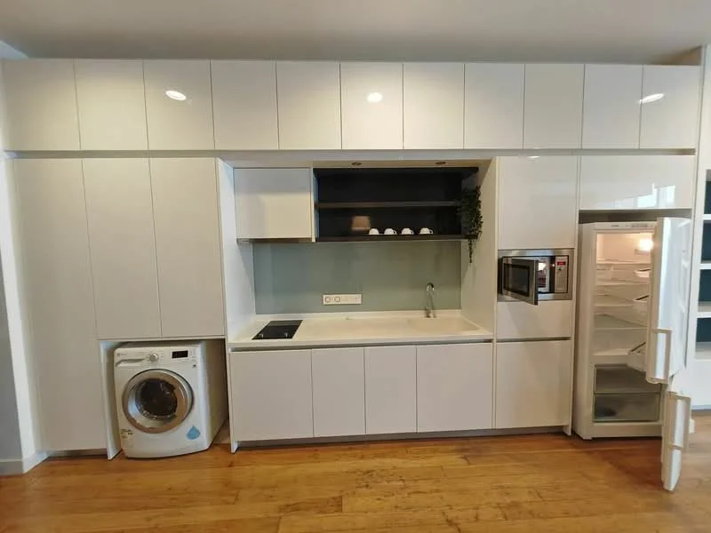 Kitchen features: white cabinetry with flat-panel doors, white countertop, single-bowl stainless-steel sink, chrome pull-down faucet, built-in microwave, freestanding refrigerator, 4-burner induction hob, washing machine, wooden flooring, recessed downlights; style: modern.