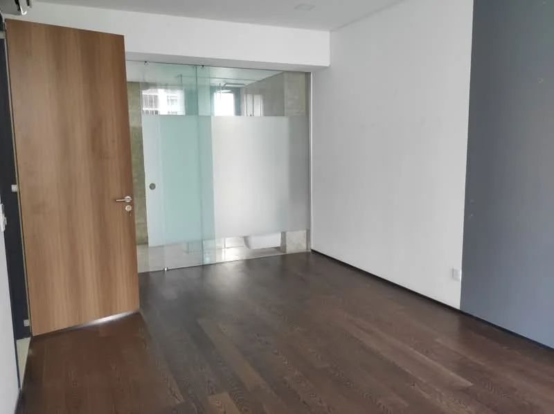Room features: dark wood flooring, white painted walls, glass partition, wooden door, natural light from windows, minimalist design; style: modern.