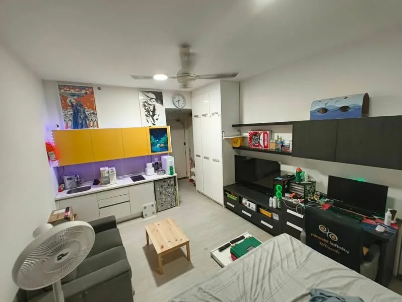 Living features: grey fabric sofa, wooden coffee table, white painted walls, light wood flooring, ceiling fan, wall-mounted TV, black cabinetry, yellow cabinetry, purple backsplash, kitchenette with sink, microwave, refrigerator, decorative wall art, clock on wall, open shelving; style: modern.