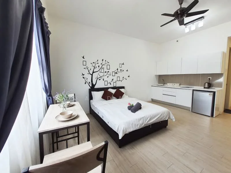Bedroom features: queen-size bed with white bedding, decorative throw pillows, wooden bedside table, wall-mounted tree decal, floor-to-ceiling window with sheer curtains, ceiling fan with light, laminate flooring, kitchenette with white cabinets, stainless-steel fridge, built-in countertop with sink, microwave, kettle; style: modern.
