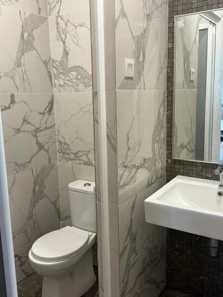 Bathroom features: white toilet, single-sink vanity with white cabinet, chrome basin mixer, framed mirror, marble tile wall cladding, grey mosaic tile flooring, recessed lighting; style: modern.