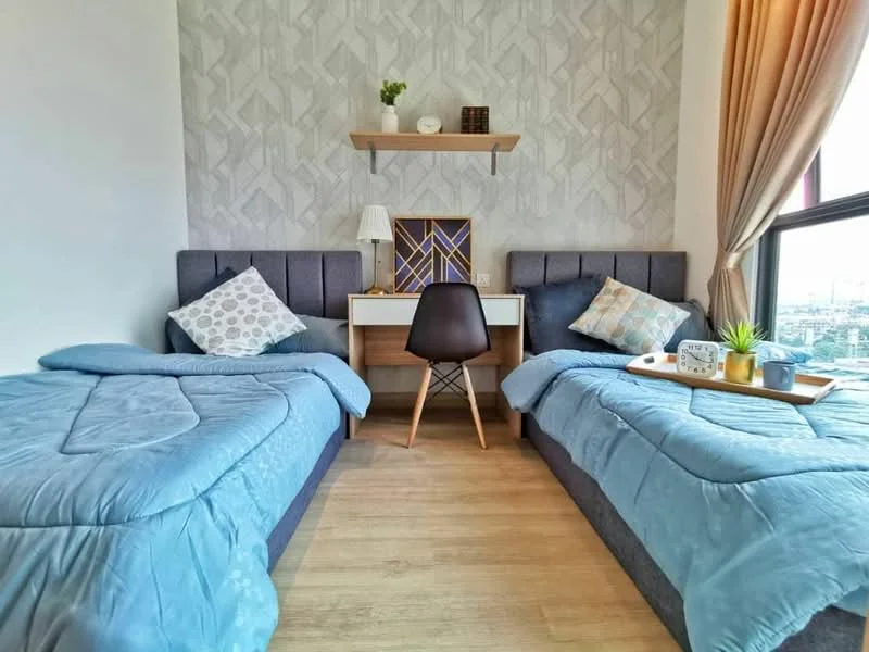 Bedroom features: two single beds with blue bedding, grey upholstered headboards, wooden study desk, black chair, decorative wall shelf, framed artwork on wall, curtains in light brown, lampshade on bedside table, wooden flooring, geometric patterned wallpaper; style: modern; view: city.