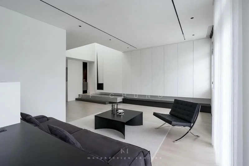 Living features: white painted walls, light wood flooring, recessed downlights, floor-to-ceiling windows, minimalist black sofa, black lounge chair, white area rug, built-in cabinetry, open layout, neutral color palette; style: modern.