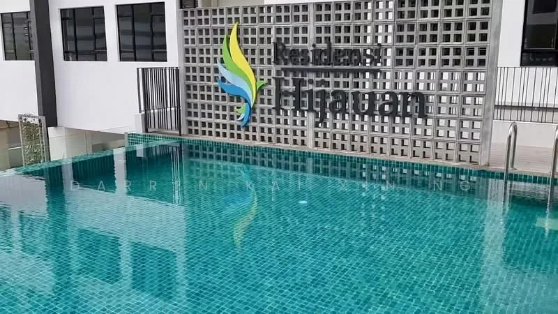 Exterior type: swimming pool deck; features: rectangular swimming pool, tiled pool surface with mosaic pattern, poolside railing, decorative feature wall with logo, water feature, surrounding deck area, green landscaping in background; style: modern.