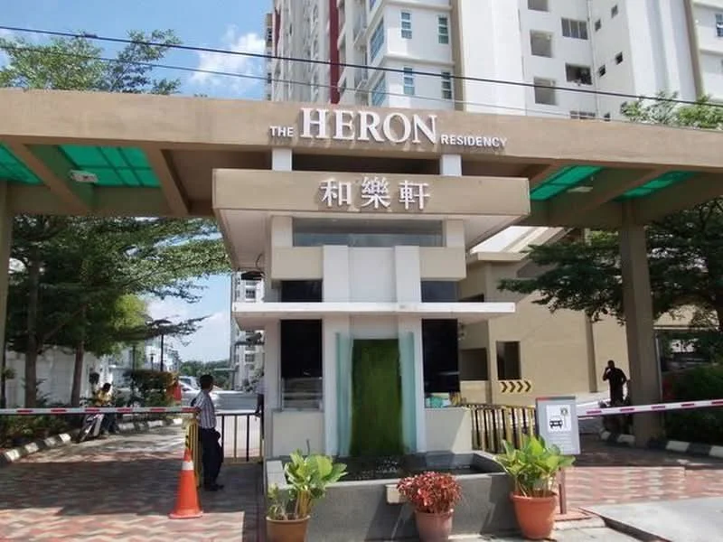 Exterior type: low-rise apartment block; features: main entrance gate, water feature at entrance, paved walkway, landscaped planters, security guard house, surrounded by greenery, signage with building name, parking area visible; style: modern.