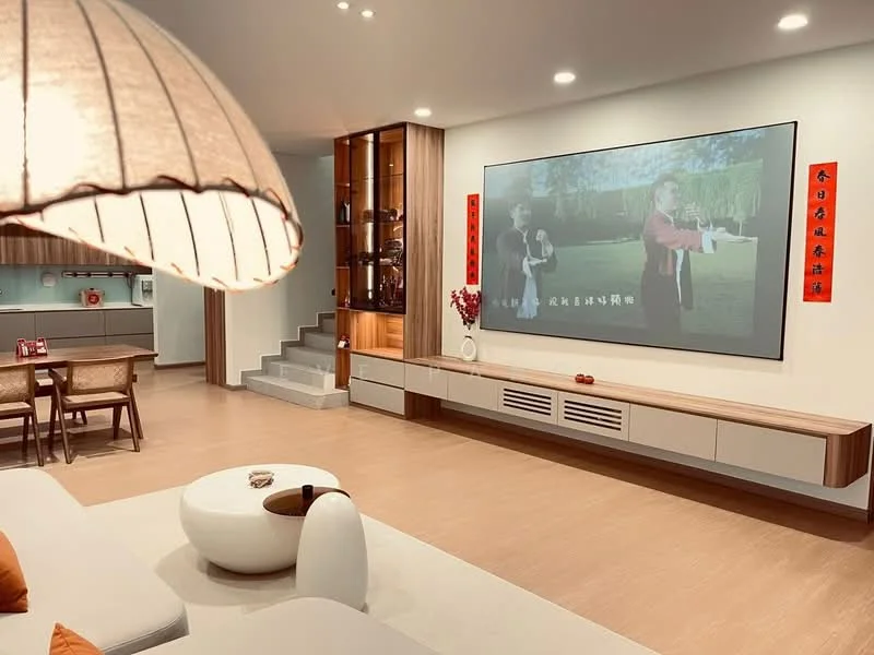 Living features: light wood flooring, white painted walls, built-in cabinetry with glass display, large wall-mounted screen, sofa with orange cushions, round coffee table, decorative wall art, recessed lighting, staircase with wooden steps, shelves with decorative items; style: modern.