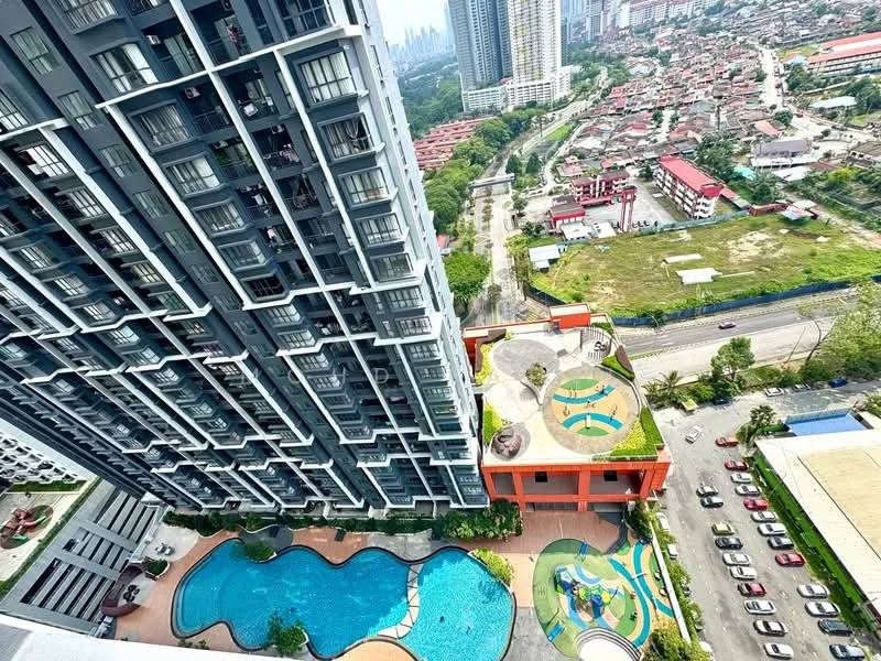 Exterior type: high-rise condominium; features: infinity pool, children's playground, landscaped garden, pool deck with loungers, manicured lawn, surrounded by mature greenery, parking lot, multiple levels of the building, urban context with city skyline in background; style: modern.