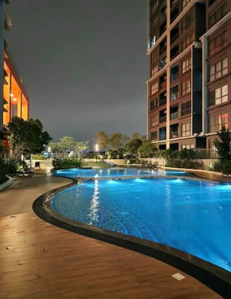 Exterior type: high-rise condominium; features: infinity pool, pool deck with loungers, landscaped garden, mature trees, ambient lighting, curved pool design, surrounding greenery, nighttime illumination; style: modern.