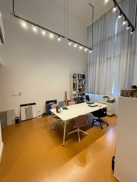 Study features: wood flooring, white painted walls, high ceiling, large windows with sheer curtains, track lighting, desk with white tabletop, pink office chairs, black office chair, bookshelf with books, printer, file storage unit; style: modern.