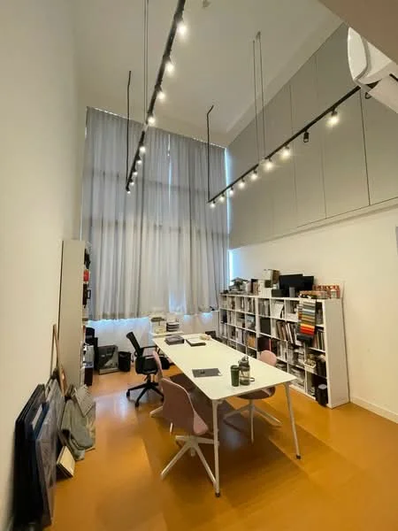 Study features: high ceiling, large windows with sheer curtains, white painted walls, wooden flooring in orange hue, suspended track lighting, long white table, pink chairs, bookshelves with various items, office chair, air conditioning unit; style: modern.