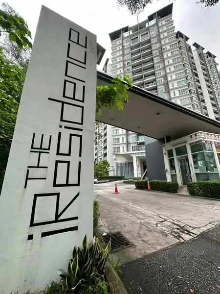 Exterior type: high-rise condominium; features: modern facade with glass and concrete, entrance with canopy, landscaped greenery at entrance, security guardhouse, paved driveway, signage with 'iP The Residence', surrounded by trees, multi-storey building, visible balconies, parking area; style: modern.