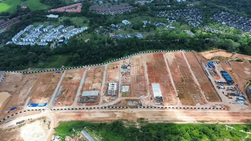 Exterior features: undeveloped land, construction site, cleared earth, scattered construction materials, road infrastructure, surrounding greenery, adjacent residential area, visible building foundations, temporary structures, marked plots for future development.
