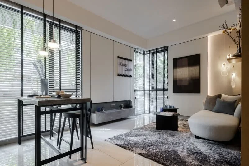 Living features: white painted walls, grey accent wall, polished tile flooring, floor-to-ceiling windows, blackout blinds, 3-blade ceiling fan, pendant lighting, area rug with geometric pattern, sofa in light grey, small dining table with 2 stools, decorative wall art, decorative vase on table; style: modern; view: garden.