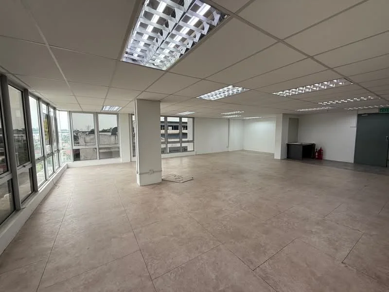Room features: large open space, tile flooring, white painted walls, drop ceiling with fluorescent lights, floor-to-ceiling windows, city view, multiple electrical outlets, air conditioning vents; style: modern; view: city.
