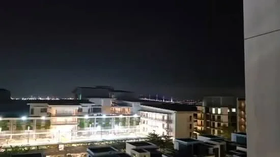 Exterior features: night view of city skyline, multiple low-rise buildings, street lighting visible, landscaped area in foreground, bridge visible in distance; style: modern.