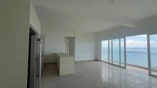 Living features: floor-to-ceiling windows, ocean view, white painted walls, polished marble flooring, high ceiling, open layout, recessed downlights, kitchen island, neutral color palette; style: modern; view: sea.