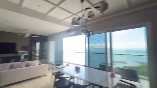 Living features: floor-to-ceiling windows, ocean view, cream painted walls, tray ceiling, chandelier, 3-seater fabric sofa in light color, dining table with black chairs, TV console, recessed downlights; style: modern; view: sea.