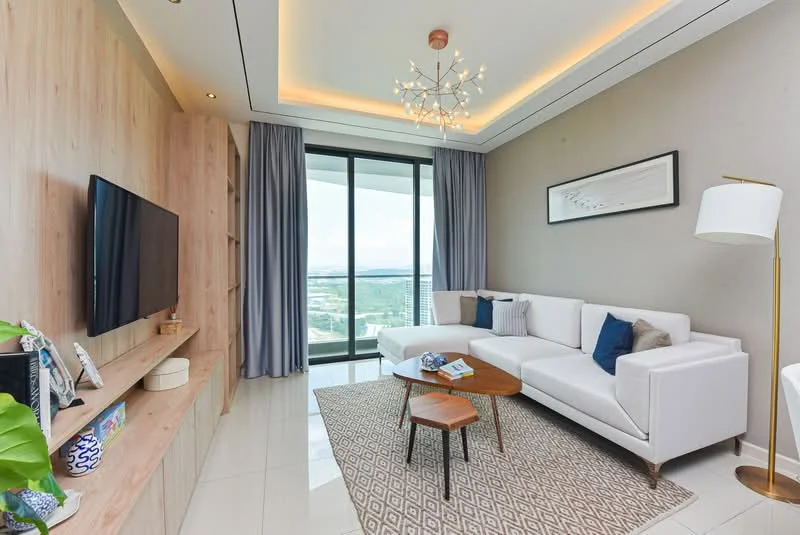 Living features: white fabric L-shape sectional sofa, wooden coffee table, area rug with geometric pattern, wall-mounted TV, light wood media console, floor-to-ceiling windows, sheer curtains, recessed downlights, chandelier with multiple bulbs, decorative wall art, greenery in ceramic pot; style: modern; view: city.