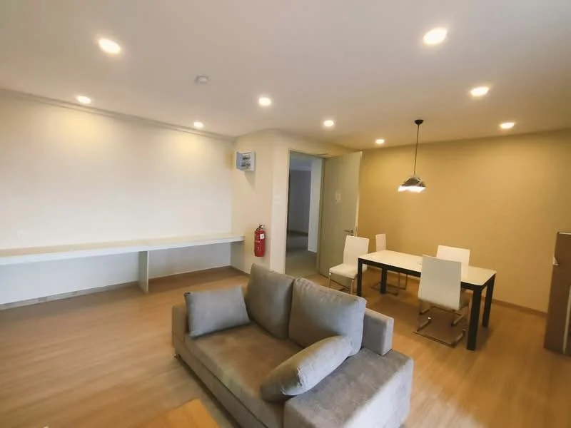 Living features: 3-seater fabric sofa in grey, wooden flooring, recessed LED downlights, white painted walls, dining table with 4 white chairs, fire extinguisher, open layout, wall-mounted air conditioning unit; style: modern.