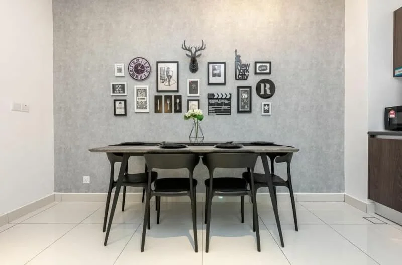 Dining features: rectangular dining table, 6 black dining chairs, grey accent wall, framed artwork on wall, decorative wall-mounted antlers, white flower arrangement in vase, white tiled flooring, built-in cabinetry, black countertop, refrigerator visible in background; style: modern.